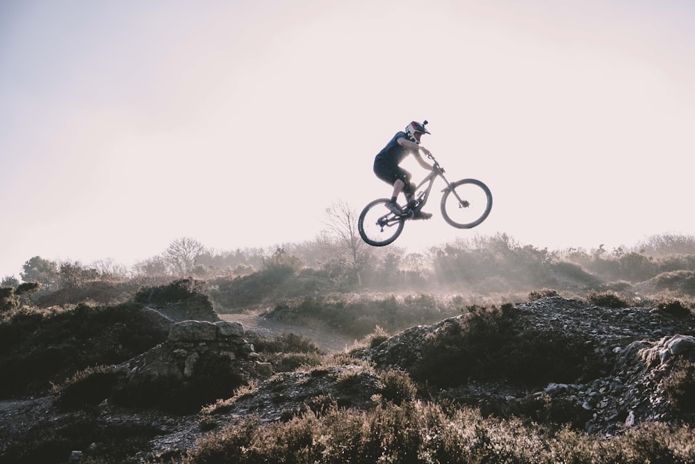 photography of man riding mountain bike jumping over ground during daytime