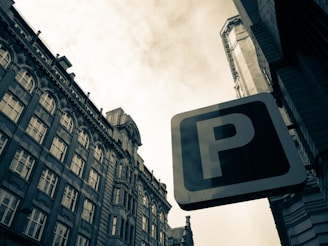 A large parking sign is prominently displayed against a backdrop of tall, ornate buildings featuring numerous windows and intricate architectural details. The sky is overcast, giving the scene a slightly muted appearance.
