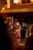 A street musician performs in front of a warmly lit French bakery titled 'Boulangerie Saint Michel'. The artist is dressed in colorful clothing, playing a guitar and singing into a microphone.