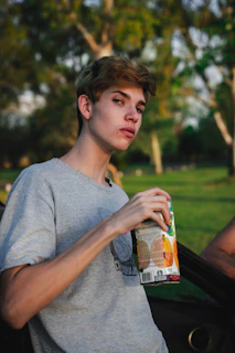 A cheerful person holding a green detox juice with a sunny park background