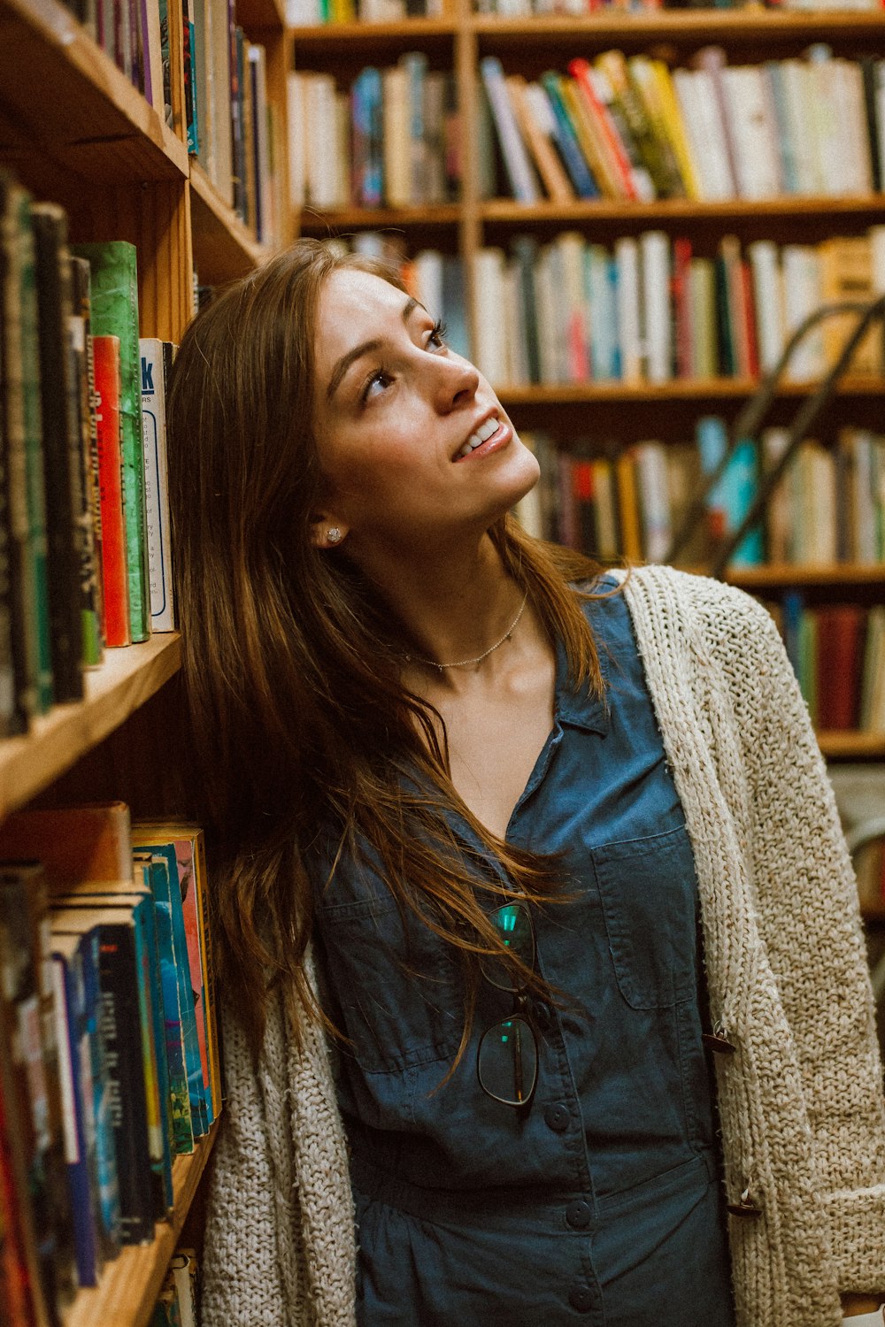 donna in cardigan che si appoggia alla libreria