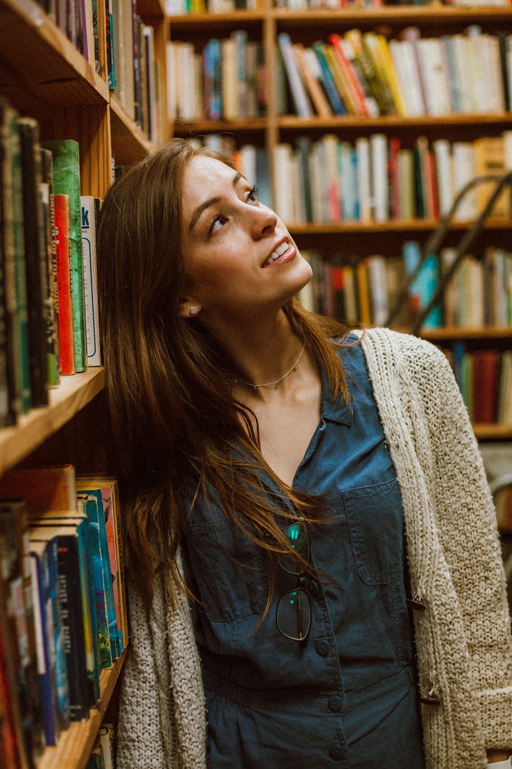 woman in cardigan leaning on bookshelf