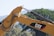 A close-up view of a construction vehicle's hydraulic arm, painted in yellow with the CAT logo prominently visible. In the background, there are blurred trees and mountains, suggesting an outdoor environment.