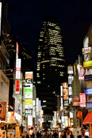 A lively city street at night, illuminated by neon signs and the hum of local nightlife.
