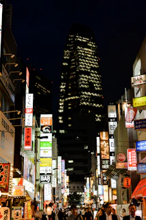 A nighttime cityscape with neon signs glowing and people strolling the lively streets.