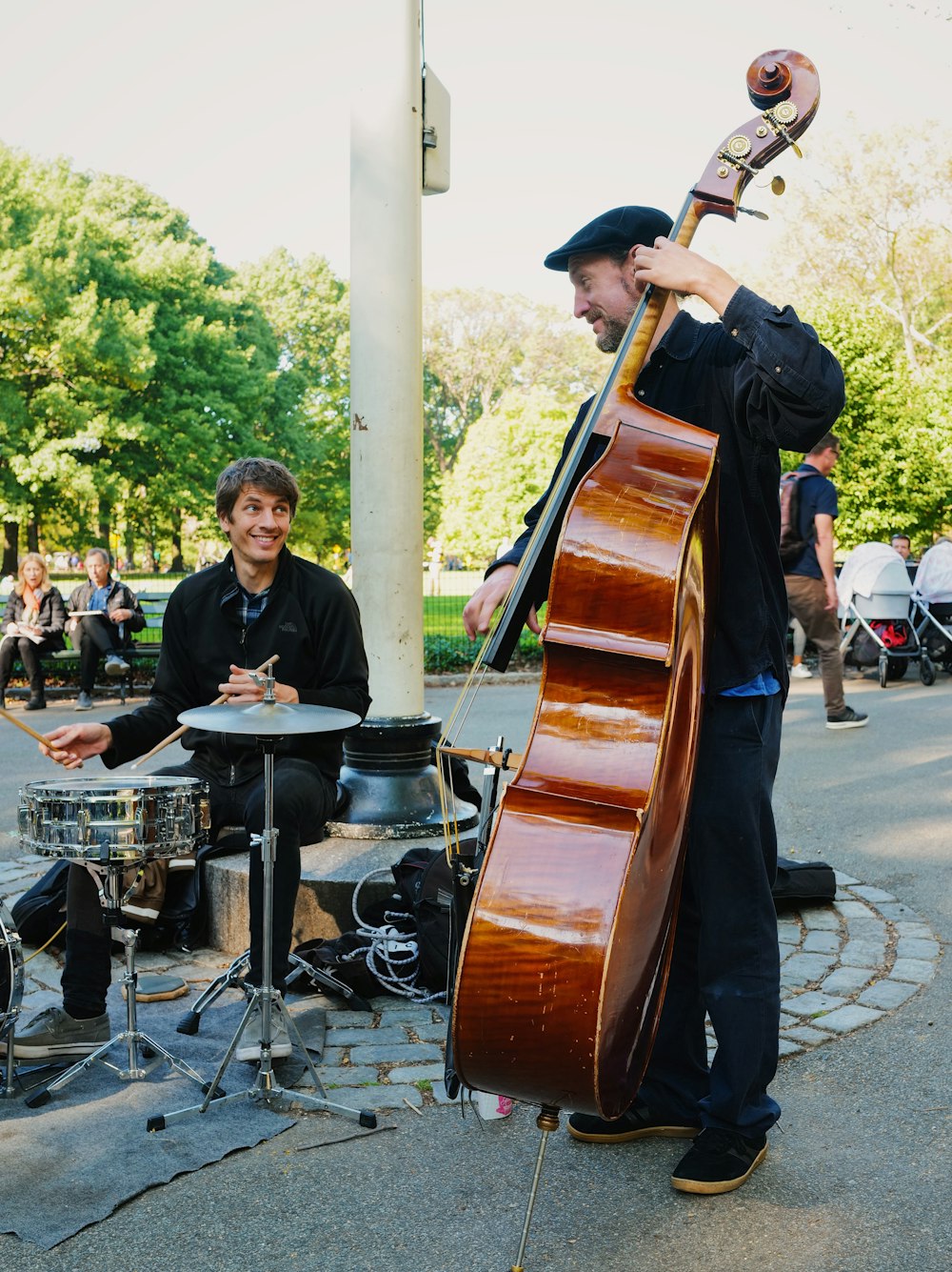 man playing cello by man playing drum at daytime