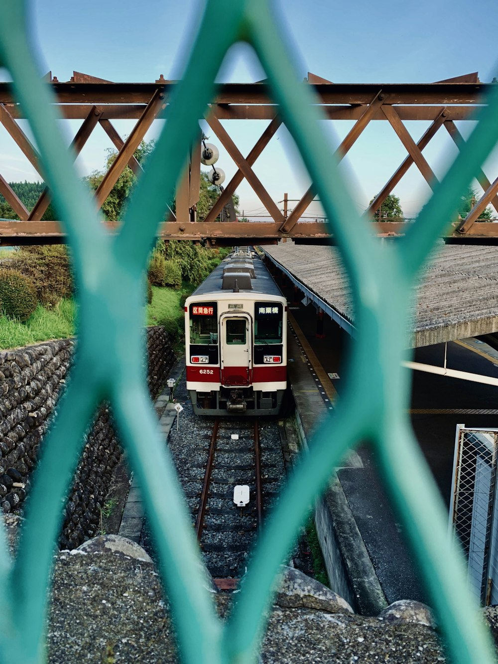 white and multicolored train under red metal bridge