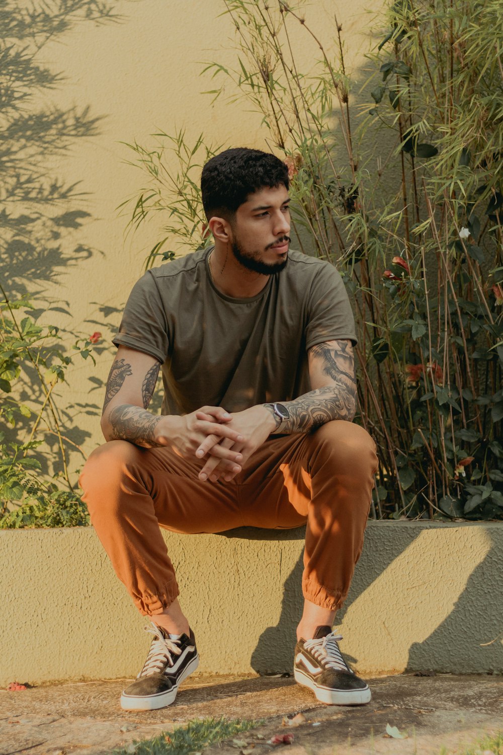 man wearing brown crew-neck long-sleeved shirt and brown pants while sitting on pavement