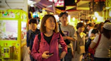 A smiling woman using a digital wallet app on her phone in a bustling market.