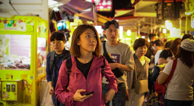 A smiling woman using a digital wallet app on her phone in a bustling market.