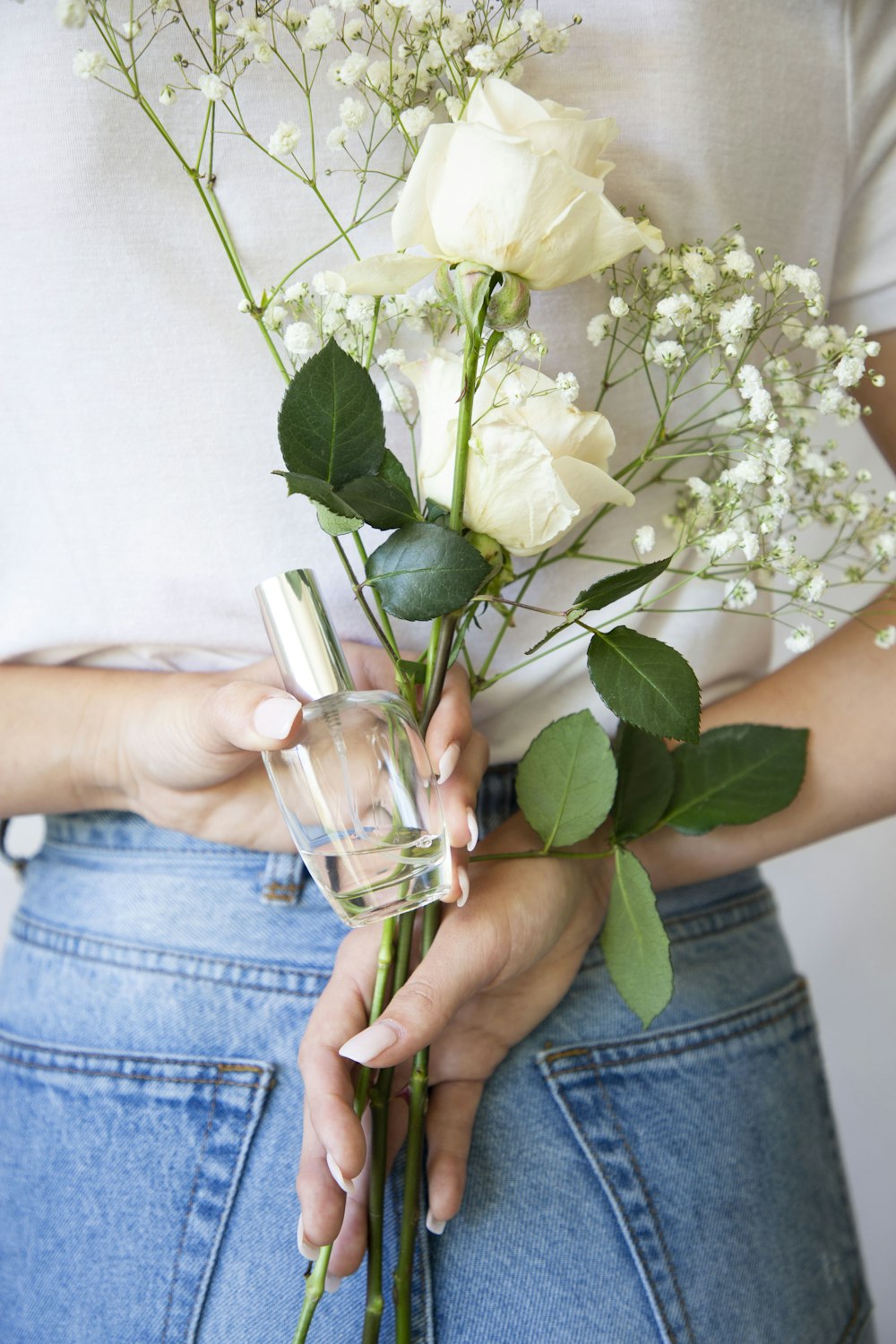 person holding white rose and clear glass bottle