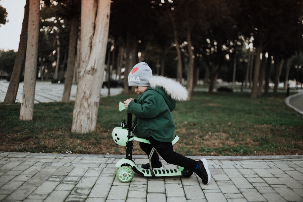 a little boy riding a green scooter on a sidewalk