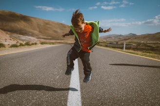 a young boy is jumping in the air on a road