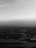 A grayscale aerial view of a landscape featuring numerous bodies of water, possibly lakes, scattered across a seemingly flat terrain. The horizon is visible in the distance with a subtle gradation in the sky.