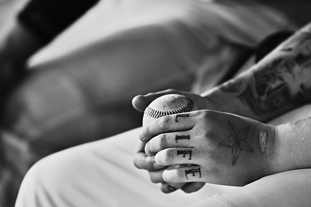 fotografia em tons de cinza da pessoa segurando a bola de beisebol