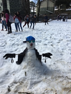 A playful snowman wearing ski goggles and a beanie on the mountain base.