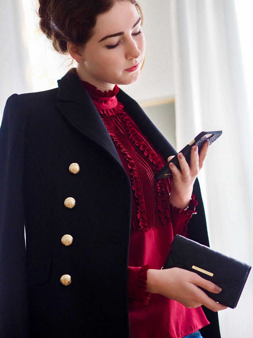 woman wearing red long-sleeved blouse with black blazer holding smartphone and wallet