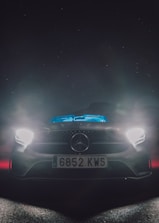 A sleek car illuminated by vibrant LED headlights on a dark road.
