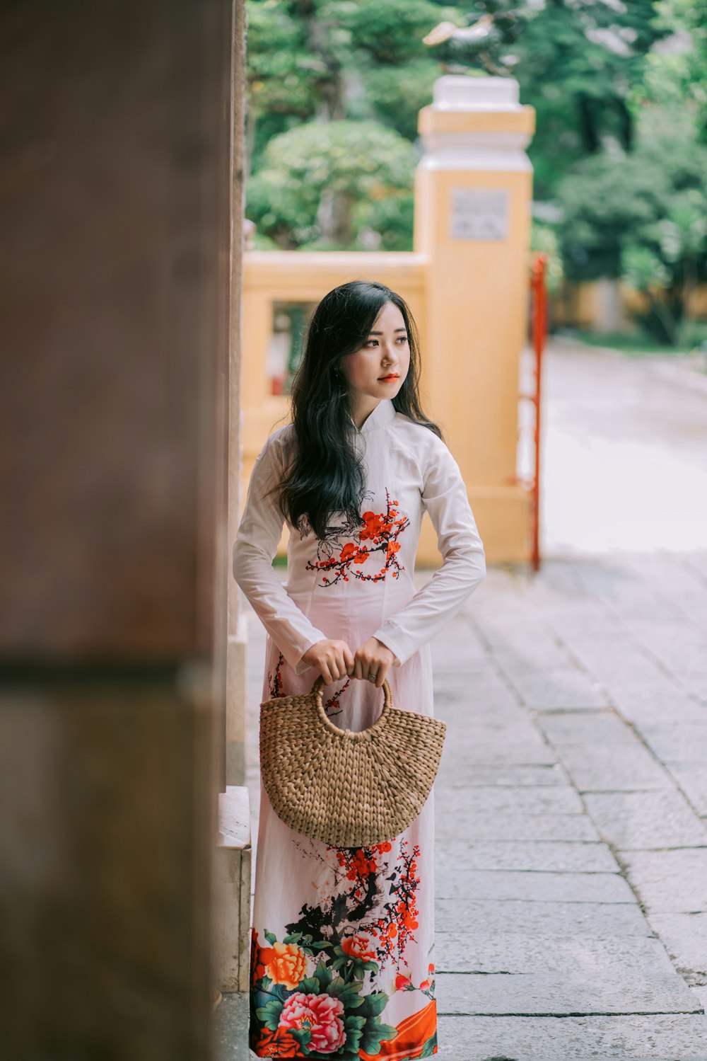 woman wearing multicolored floral dress holding beige handbag