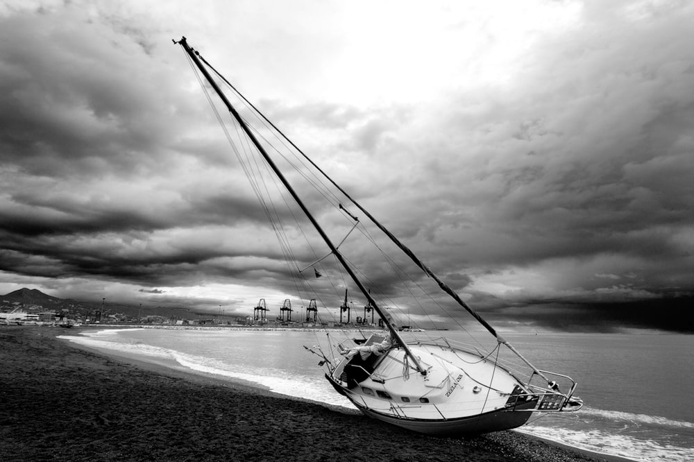 fotografia in scala di grigi di una barca a vela in riva al mare