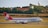 A large cargo airplane on a runway with a landscape of fields, trees, and buildings in the background. The plane has a red tail with a logo and the word 'cargolux' on its body.