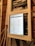 A close-up view of an electrical panel with a digital screen displaying a spreadsheet. The panel is secured with masking tape, and various colored wires are visible. The wooden wall in the background provides a rustic contrast to the modern equipment.
