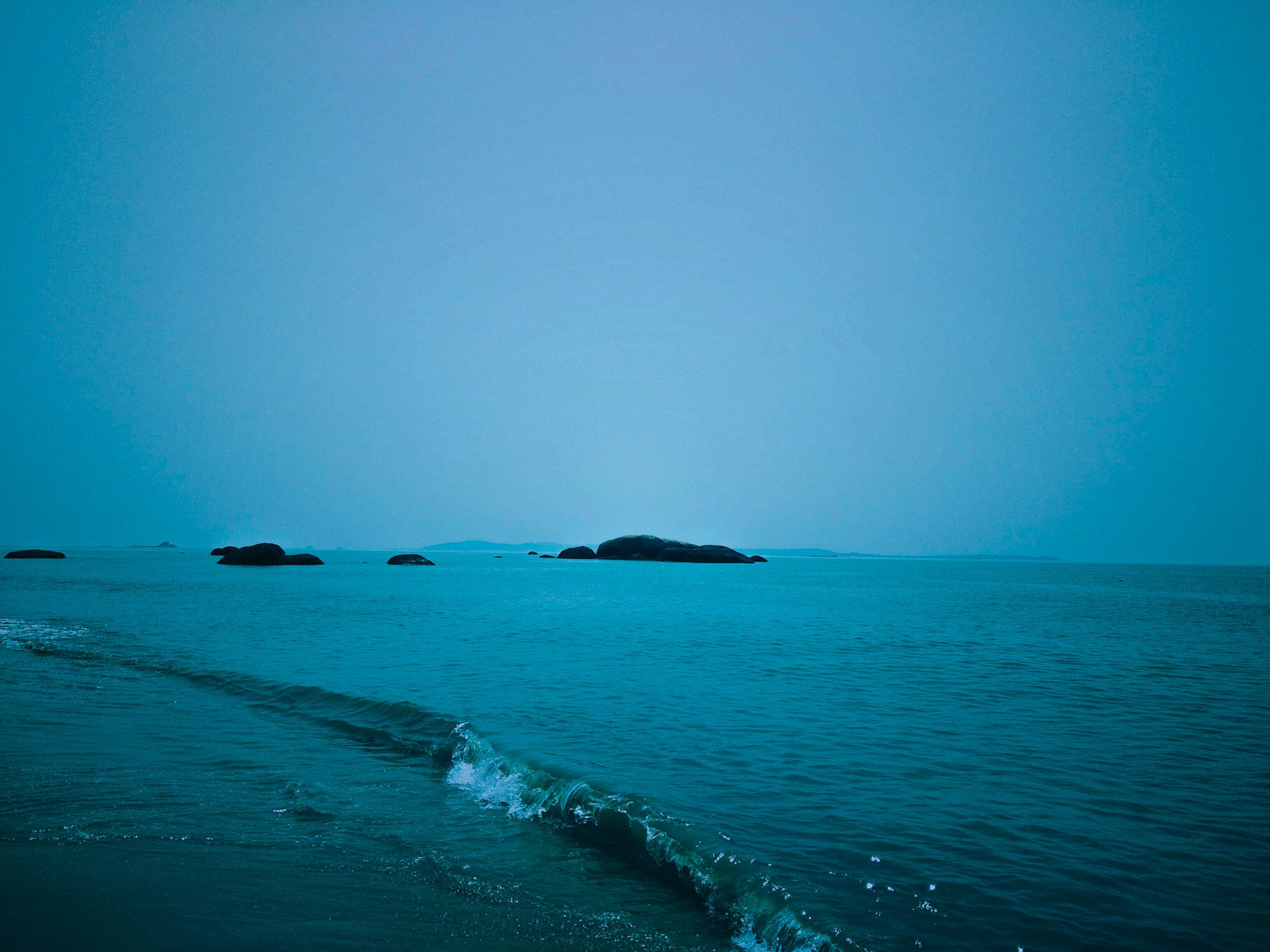 A tranquil sea view with gentle waves lapping against smooth rocks under a clear blue sky.