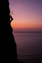 A climber silhouetted against a fiery sunset while reaching the summit.