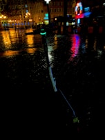 Evening shot of a glowing electric unicycle parked near a city park bench, lights reflecting on wet pavement.