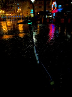 Evening shot of a glowing electric unicycle parked near a city park bench, lights reflecting on wet pavement.