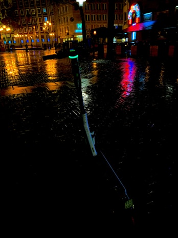 A nighttime city scene with a glowing green electric scooter parked near a café.
