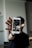 A person holds a smartphone displaying a social media profile with photos. The focus is on the phone with the individual's profile interface visible, set against a blurred background.