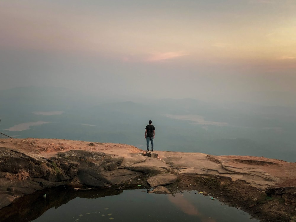 man standing on rock near body of water at daytime