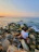 A serene photo of a person wearing a soft green t-shirt sitting peacefully by the ocean at sunset.