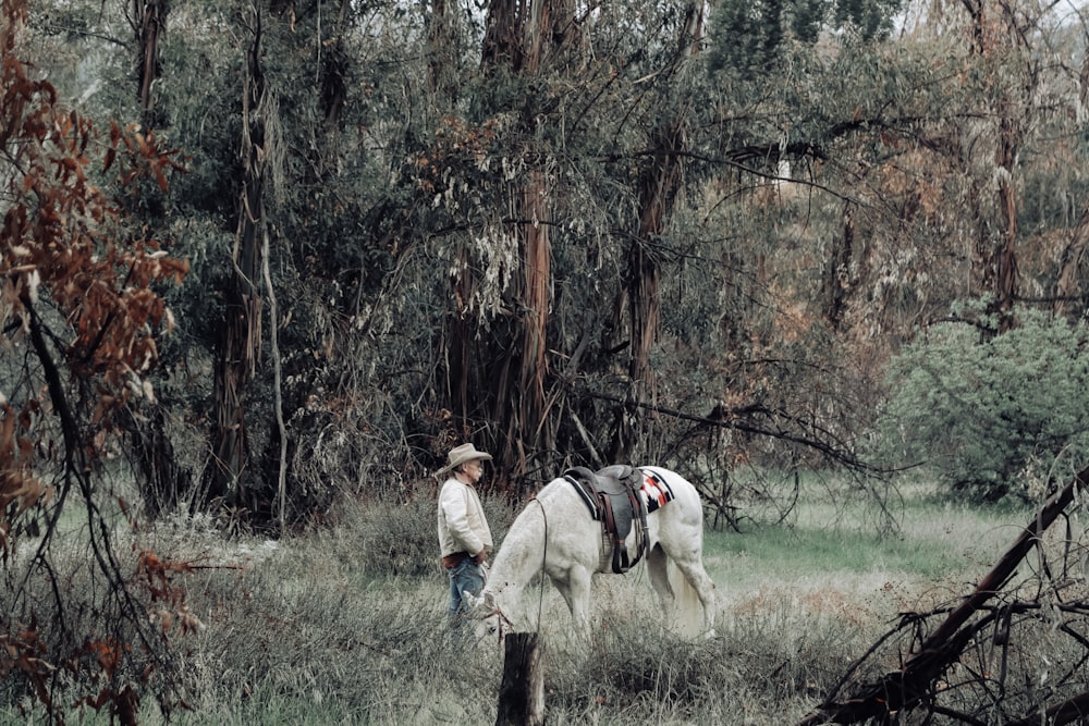 man standing beside white horse and trees