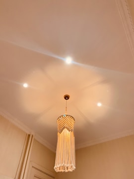 A ceiling-mounted pendant light with a long, fringed lampshade made of woven material. Soft, warm lighting creates a cozy atmosphere in the room, accentuated by additional small, recessed lights.