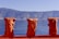 Three orange life jackets hang on a railing with a backdrop of calm blue water and mountainous terrain in the distance. The scene is set under a clear blue sky, suggesting a peaceful outdoor aquatic environment.