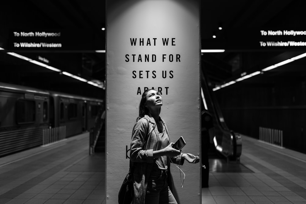 grayscale photography of woman holding Android smartphone while looking up