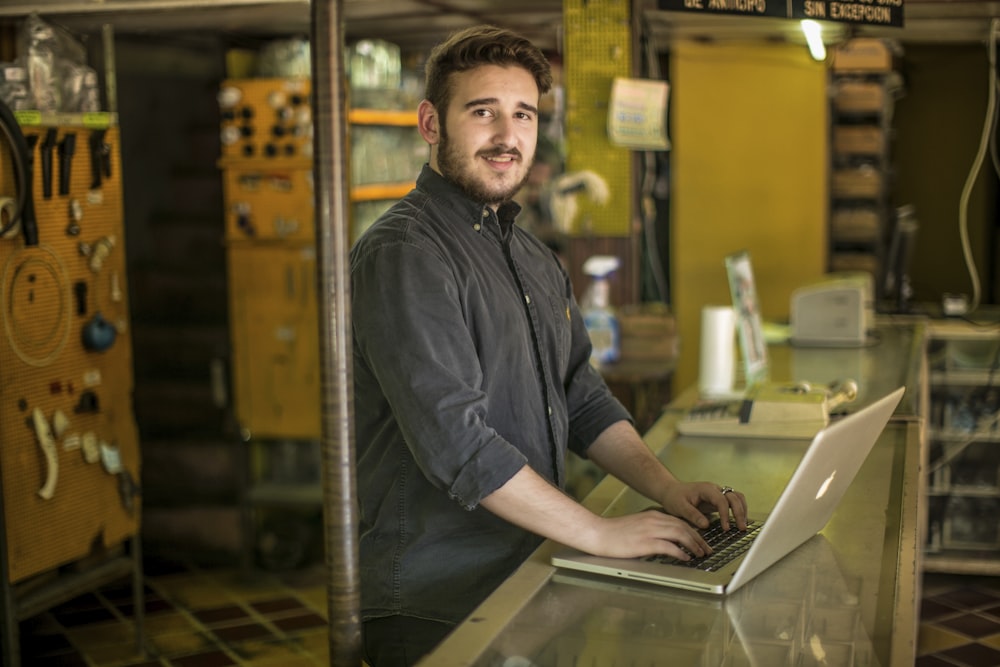 man standing and smiling while using MacBook