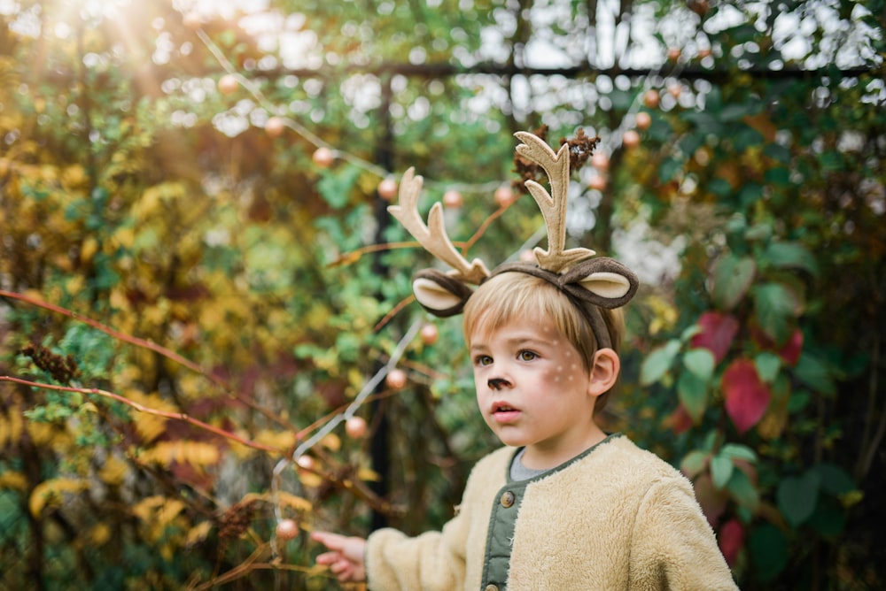 boy wearing deer head band near plants