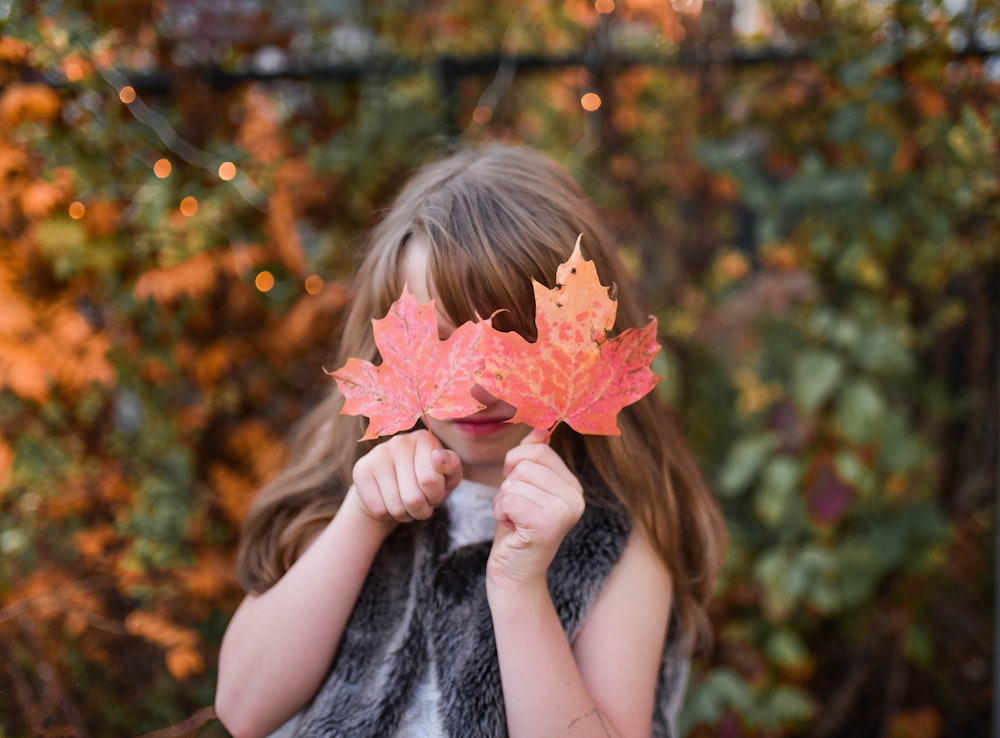 girl holding brown maple leaves