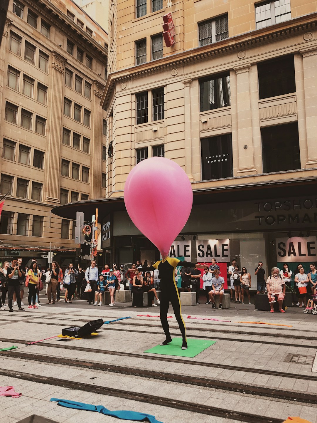 man with his head inside pink inflated balloon standing on man with his head inside pink inflated balloon standing on