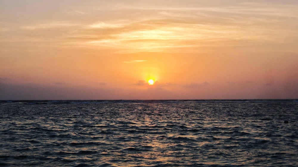 the sun is setting over the ocean on a cloudy day