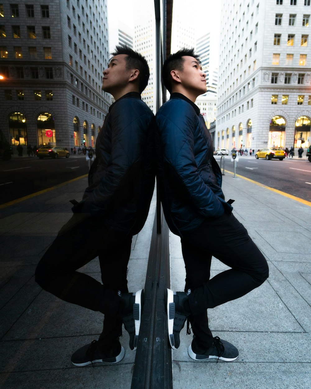 man leaning on mirrored wall wearing blue jacket