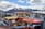A collection of old, worn vehicles with chipped paint and broken windows, arranged in a lot against the backdrop of snow-capped mountains and a partly cloudy sky.