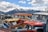 A collection of old, worn vehicles with chipped paint and broken windows, arranged in a lot against the backdrop of snow-capped mountains and a partly cloudy sky.