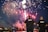 Two law enforcement officers stand by a waterfront watching a vibrant fireworks display in the night sky. The fireworks illuminate a dark, clear sky with vivid colors.