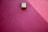 A smooth, pink plaster wall features a minimalist, rectangular light fixture casting a slanted shadow.