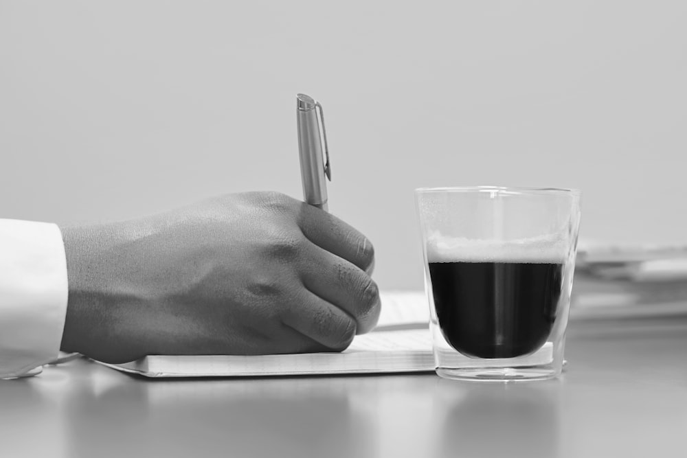 person writing on note book beside filled cup