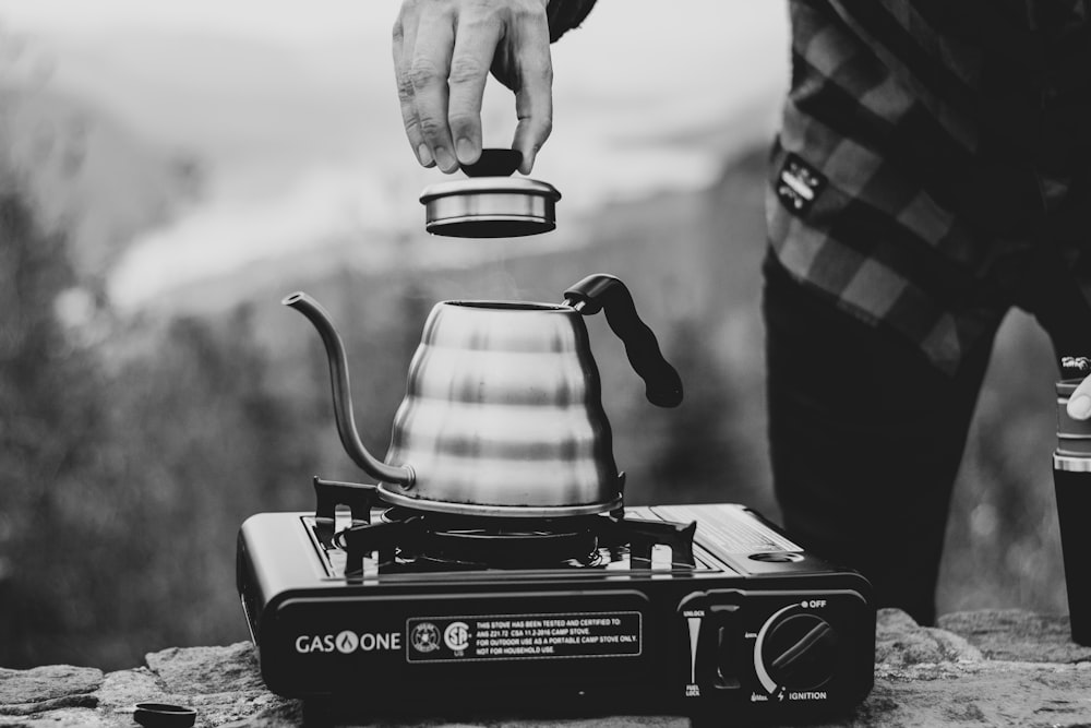 grayscale photo of person holding the lid of teapot